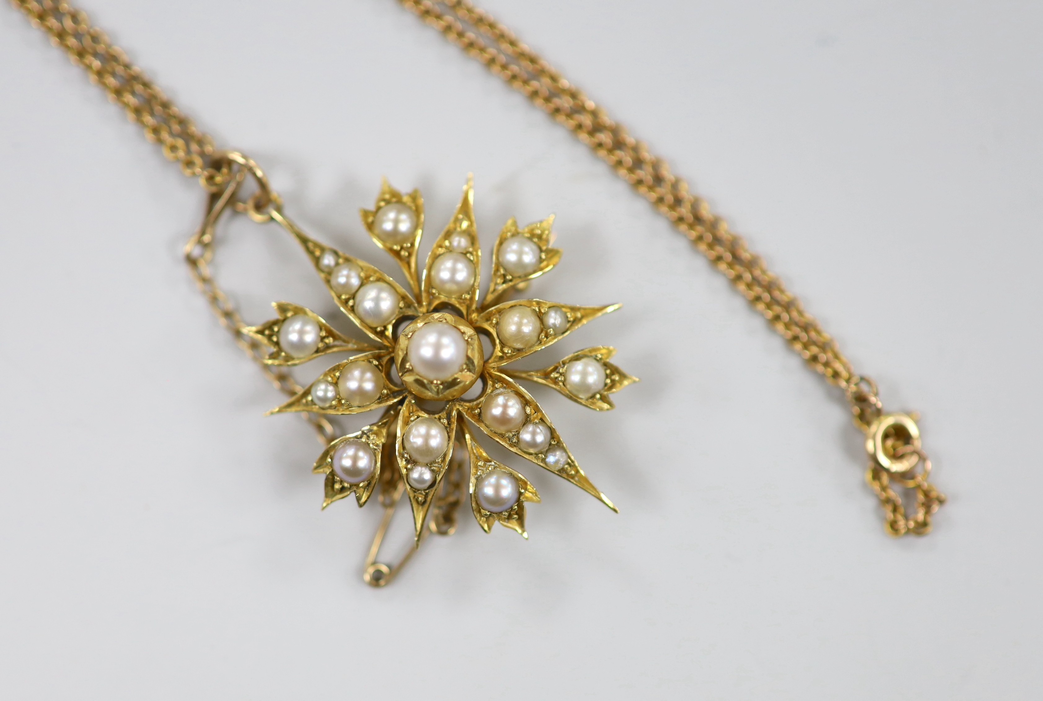 An Edwardian yellow metal and split pearl cluster set starburst pendant brooch, 37mm, on a later 9ct chain, 40cm, gross weight 9.6 grams.